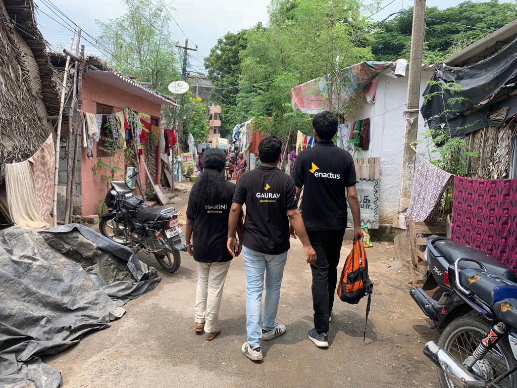 3 members of Enactus wearing the Enactus T-Shirt walking through slum area